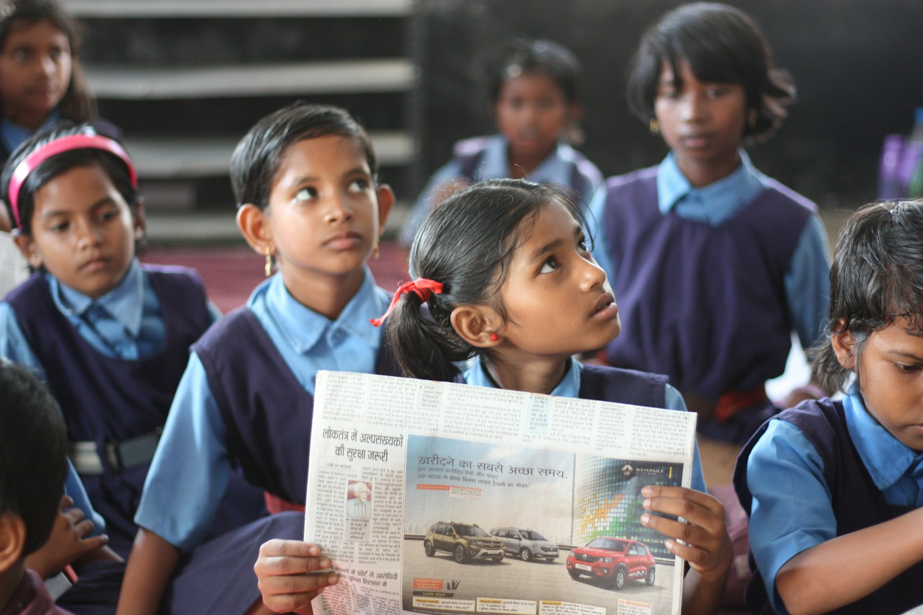Indian schoolgirls in uniform listening during class, with one student holding a newspaper